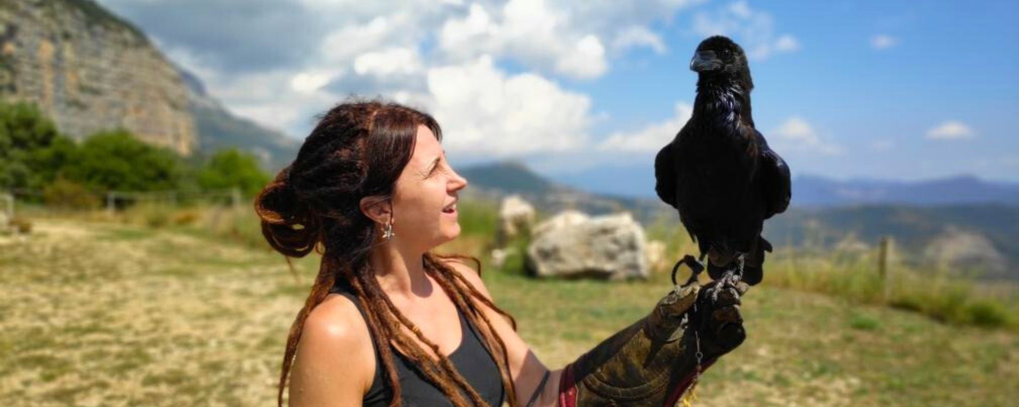 Mujer sonriente con un cuervo negro en el brazo en plena naturaleza regalos para personas especiales con animales salvajes